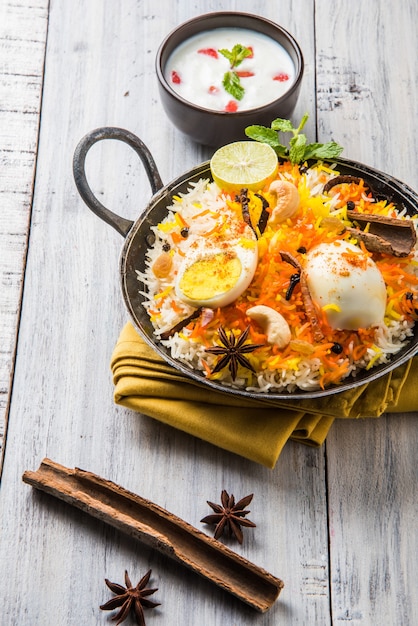 Indian Egg Biryani or anda rice served in kadhai or kadai with yogurt dip, selective focus