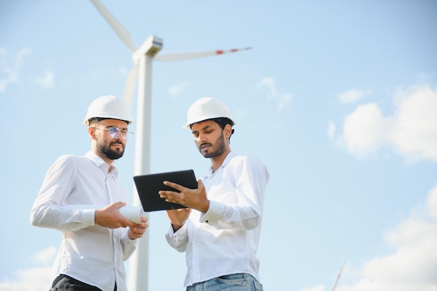 Indian and european male engineers working on wind farm with windmills