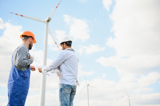 indian and european male engineers working on wind farm with windmills