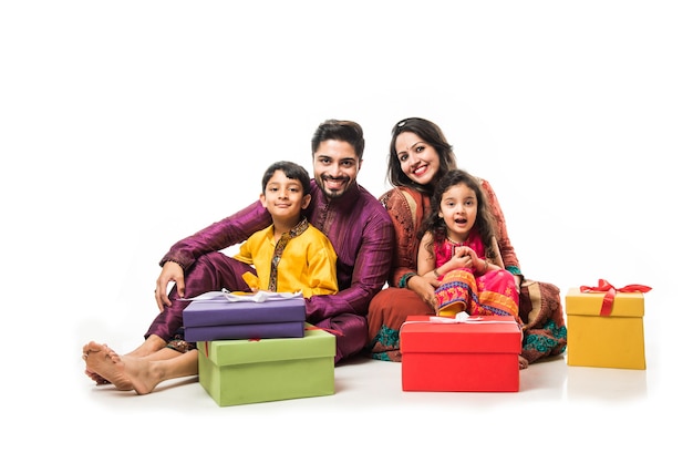 Indian family celebrating Diwali or Deepavali in traditional wear while sitting isolated over white background with gift boxes and lamp in thali