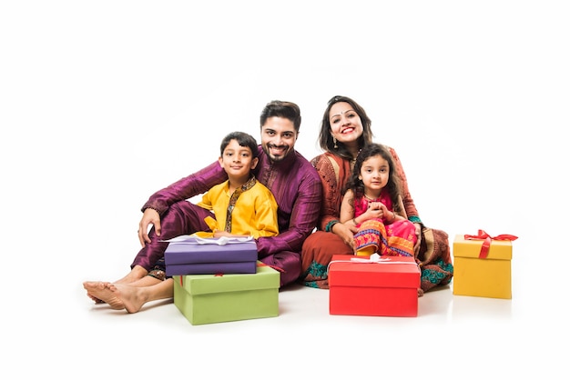 Famiglia indiana che celebra diwali o deepavali in abbigliamento tradizionale mentre è seduto isolato su sfondo bianco con scatole regalo e lampada in thali