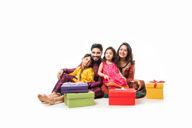 Indian family celebrating Diwali or Deepavali in traditional wear while sitting isolated over white background with gift boxes and lamp in thali