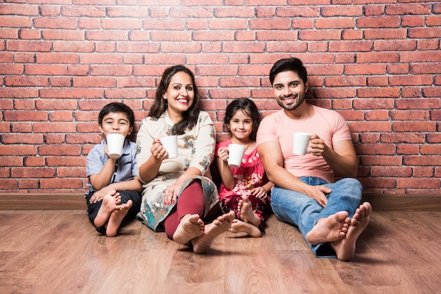 Indian family drinking milk white sitting on wooden floor against red brick wall indoors