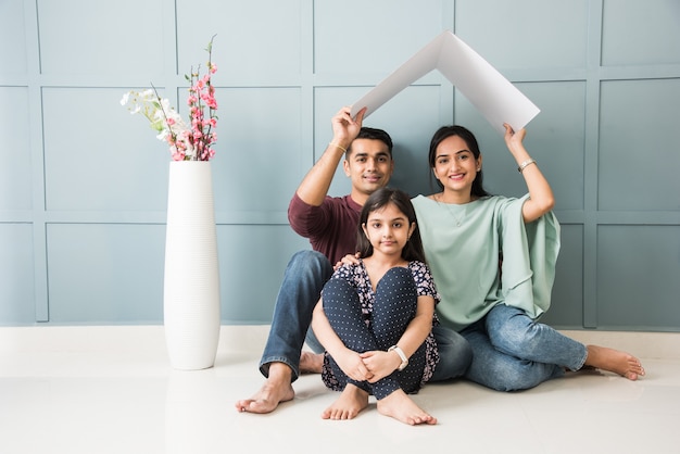 Indian family Father, mother, son and daughter holding House roof made of cardboard 