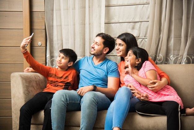 Photo indian family sitting on sofa and using smartphone laptop or tablet watching movie or surfing internet