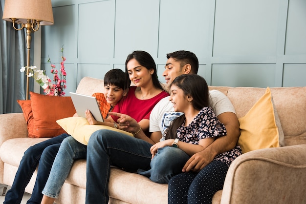 소파에 앉아 스마트 폰, 노트북 또는 태블릿을 사용하고 영화를 보거나 인터넷을 서핑하는 인도 가족