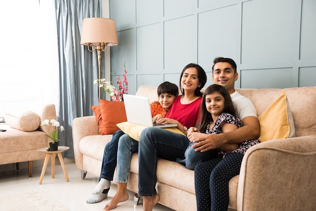 Indian family sitting on sofa and using smartphone, laptop or tablet, watching movie or surfing internet
