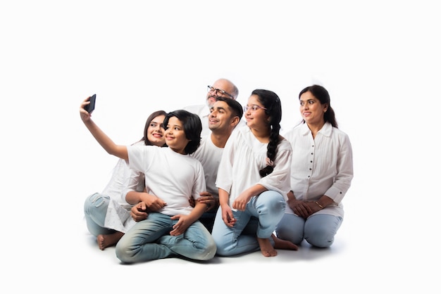 Indian family of six video calling on smartphone or taking selfie picture against white