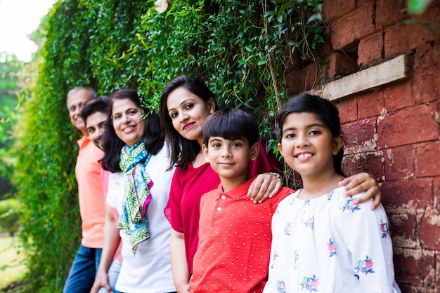 Indian family standing in line against wall covered with creepers. Multi generation of asian family in park or garden having fun, healthy family life concept