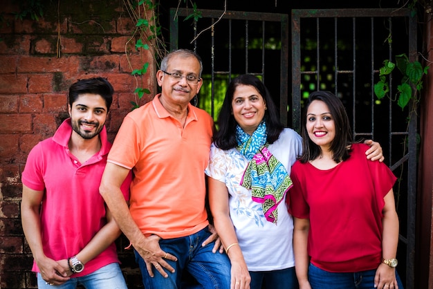 Indian family standing in line against wall covered with creepers. Multi generation of asian family in park or garden having fun, healthy family life concept