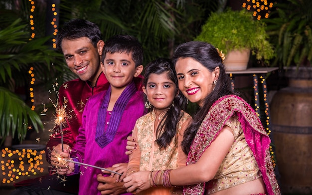 Indian Family in traditional wear playing with sparklers or phuljhadi while celebrating diwali festival, outdoor