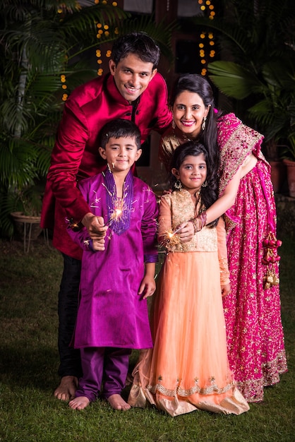 Indian Family in traditional wear playing with sparklers or phuljhadi while celebrating diwali festival, outdoor