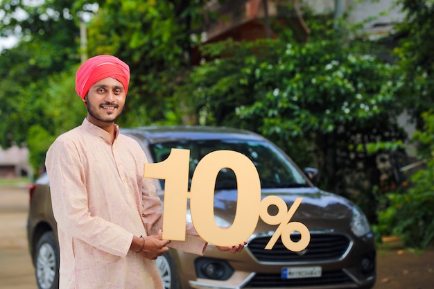 10％の看板を持って、新しい車で立っているインドの農民