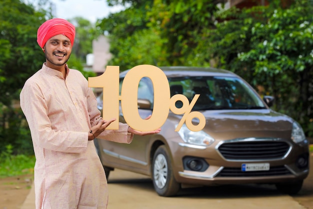 Indian farmer holding ten percent sign board and standing with new car