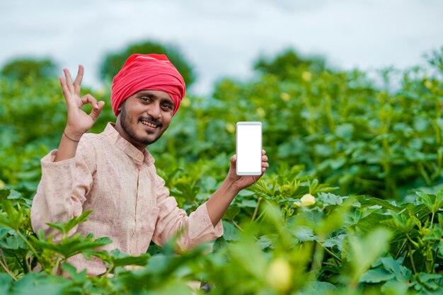 Indian farmer showing smartphone screen at agriculture field.