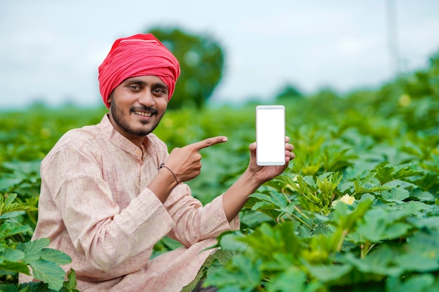 Indian farmer showing smartphone screen at agriculture field.