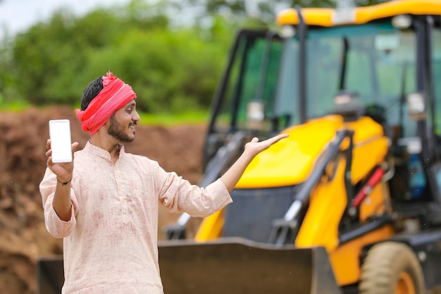 彼の新しい土工機械機器でスマートフォンを示すインドの農民
