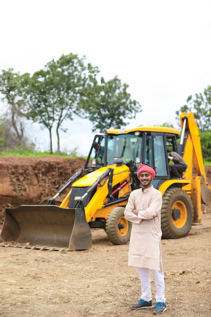 Indian farmer standing with his new earth mover machinery.