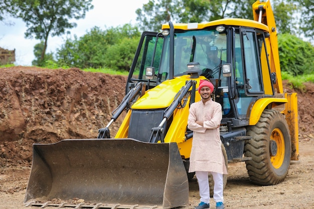 Indian farmer standing with his new earth mover machinery.