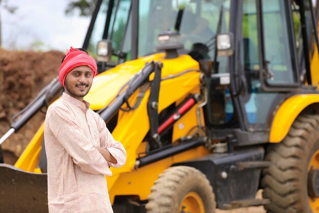 Indian farmer standing with his new earth mover machinery.