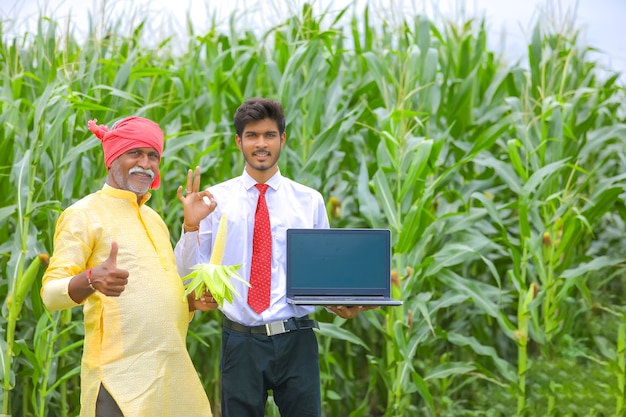トウモロコシ畑で農学者とノートパソコンの画面を表示しているインドの農民