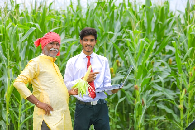 Indian farmer with agronomist at corn field and showing some information in laptop
