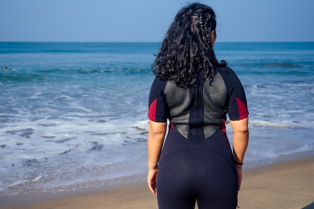 Indian female surfer dressed in black wet suit looking at sea\
back