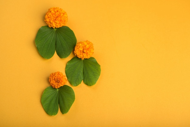 Indian Festival Dussehra, showing golden leaf (Bauhinia racemosa) and marigold flowers on a yellow background.