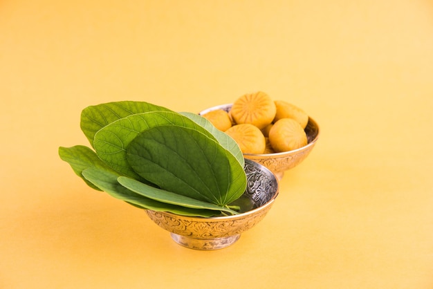 Indian festival dussehra, showing golden leaf with traditional indian sweets pedha in silver bowl on yellow background, greeting card