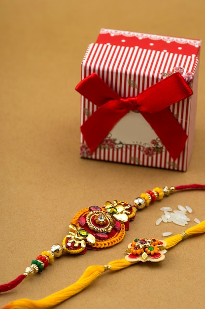 Indian festival rakhi, rice grains and gift box on orange background