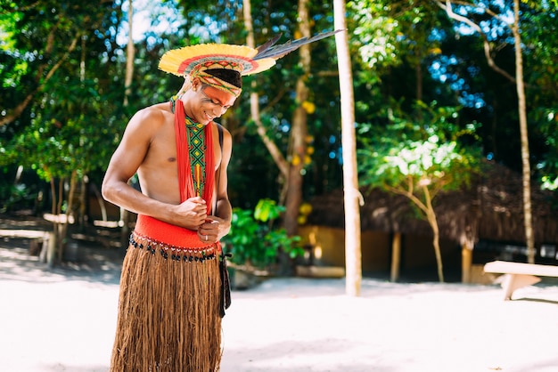 Indian from the PataxÃ³ tribe with feathered headdress looking down and smiling. Indigenous from Brazil with traditional facial paintings