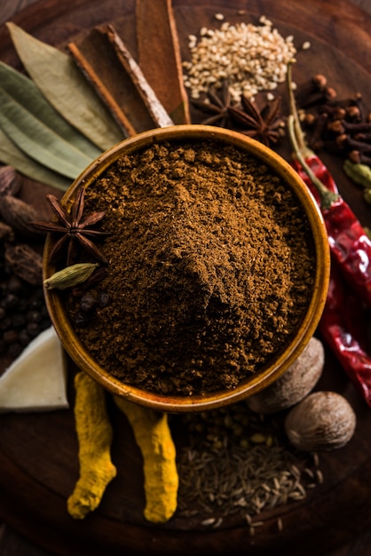 Indian Garam masala powder in bowl and it's ingredients colourful spices. Served over moody background. selective focus