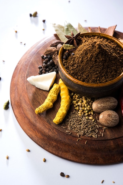 Indian Garam masala powder in bowl and it's ingredients colourful spices. Served over moody background. selective focus