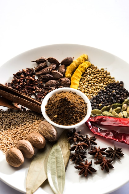 Indian Garam masala powder in bowl and it's ingredients colourful spices. Served over moody background. selective focus