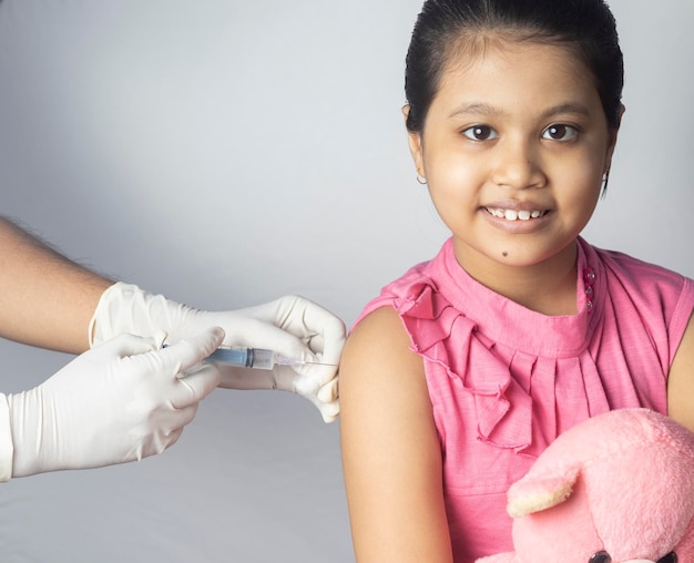Photo an indian girl child with teddy bear in lap receiving vaccine dose on white background