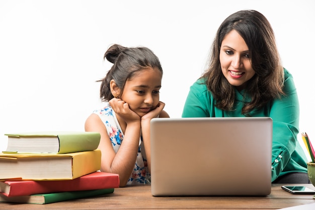 Ragazza indiana che studia con la madre o l'insegnante al tavolo di studio con computer portatile, libri e si diverte imparando