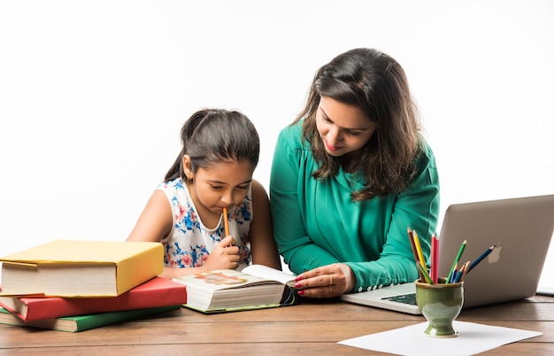 Indian girl studying with mother or teacher at study table with laptop computer, books and having fun learning