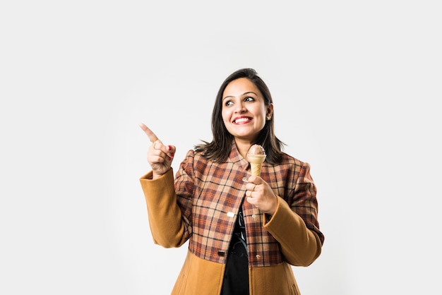 Indian girl or woman eating ice cream while wearing warm winter clothes on white background