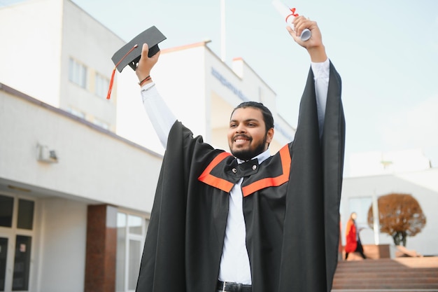 Indian graduate in graduation robe with diploma in university campus copy space