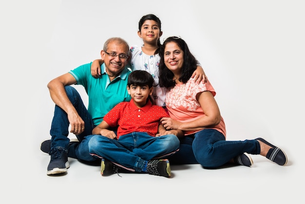 Indian Kids with grandparents smiling while sitting on a white background indoors, selective focus