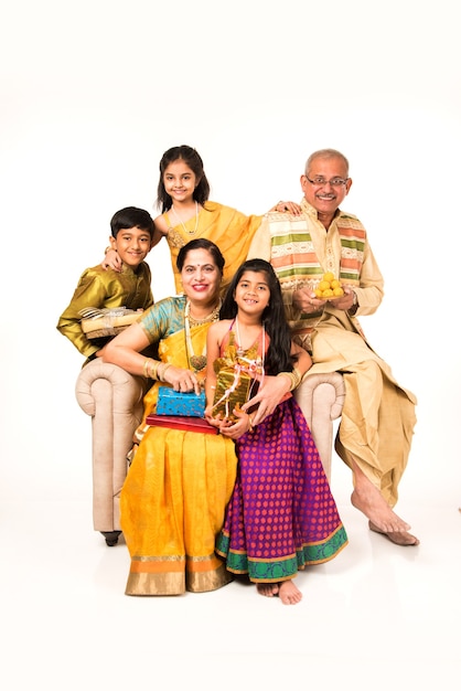 Indian kids with grandparents in traditional wear holding gifts, sweets and puja or pooja thali or taking selfie, isolated over white background