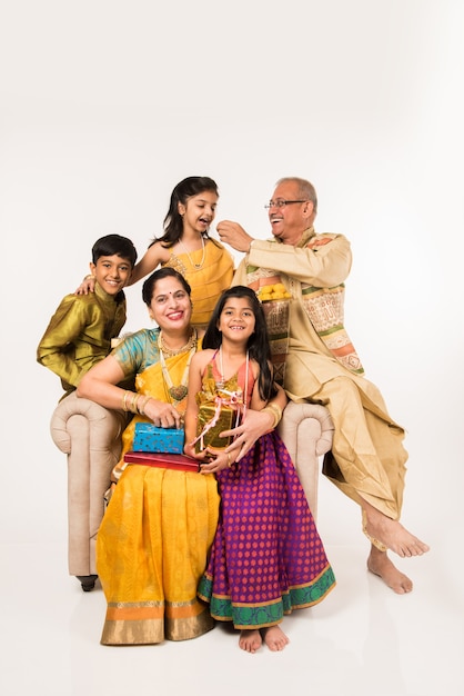 Indian kids with grandparents in traditional wear holding gifts, sweets and puja or pooja thali or taking selfie, isolated over white background