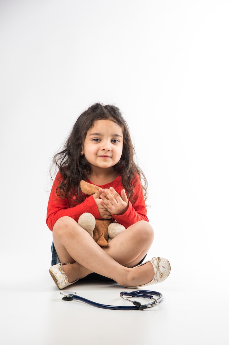 Photo indian little child girl with stethoscope and stuffed baby or puppy toy sitting against white background