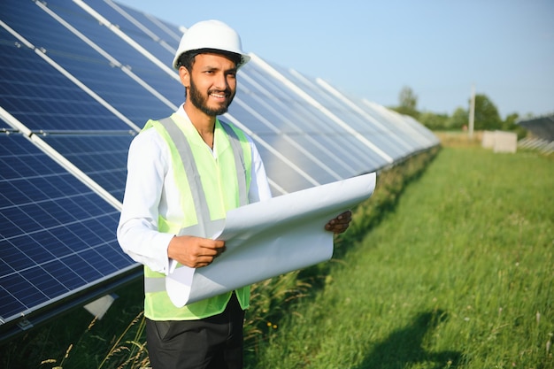 녹색 조끼를 입은 인도 남성 엔지니어가 태양 전지판의 현장에서 일하고 있습니다.
