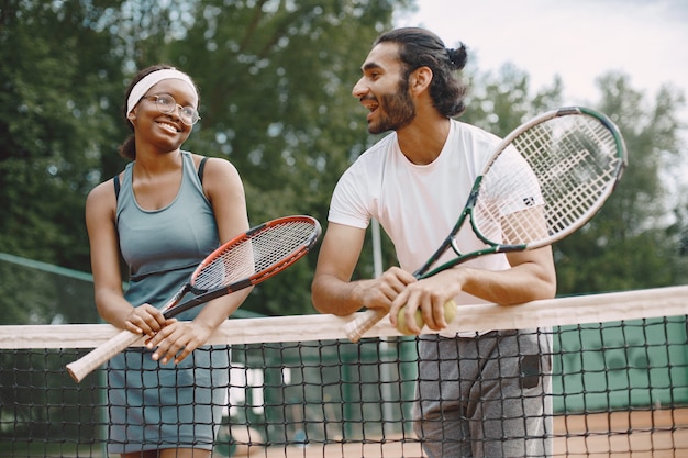 Indian man and black american woman standing on a tennis court