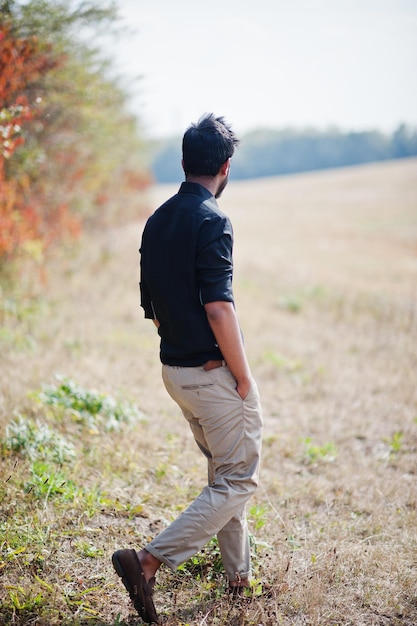 Photo indian man at black shirt and beige pants posed at field against autumn leaves