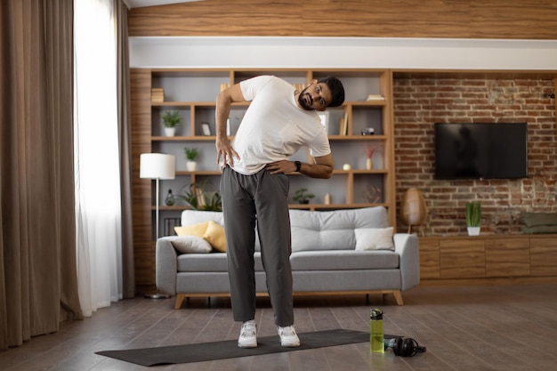 Indian man doing side tilts with hands on hips at home