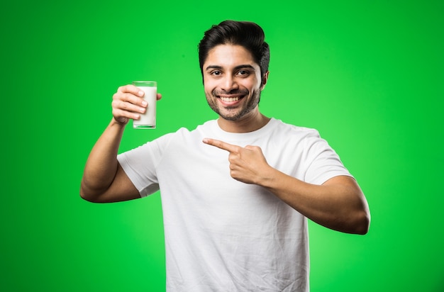 Indian man drinking milk in glass while standing isolated