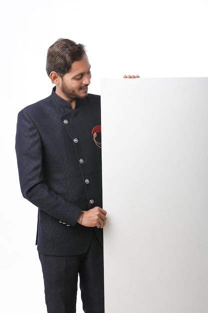 흰색 배경 위에 서 있는 전통 의상을 입고 축제 시즌에 제안을 홍보하는 화이트 보드를 들고 있는 인도 남자.
