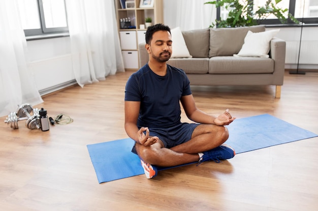 indian man meditating in lotus pose at home